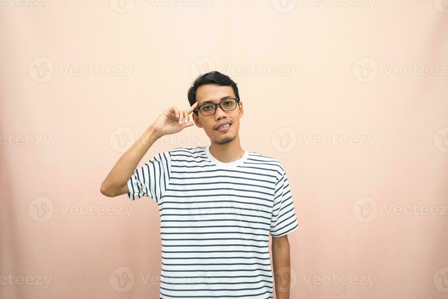 asiático hombre en lentes vistiendo casual a rayas camiseta, gesticulando obtener ideas, mirando para ideas, pensamiento. aislado beige antecedentes. foto