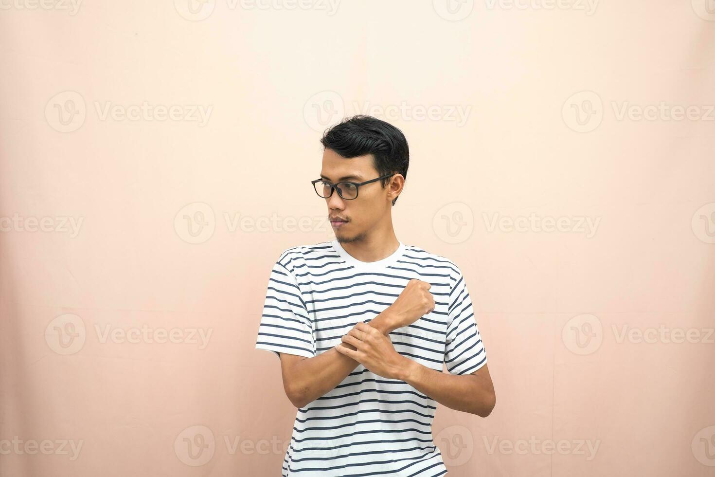 Asian man with glasses wearing casual striped shirt, fist fist pose, indicating strong or ready to fight. Isolated beige background. photo