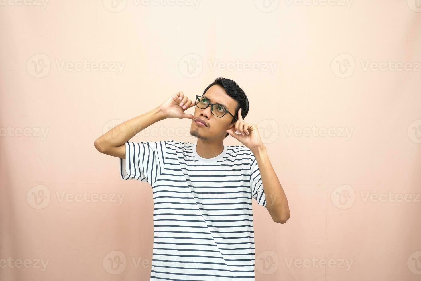 asiático hombre en lentes vistiendo casual a rayas camiseta, gesticulando obtener ideas, mirando para ideas, pensamiento. aislado beige antecedentes. foto