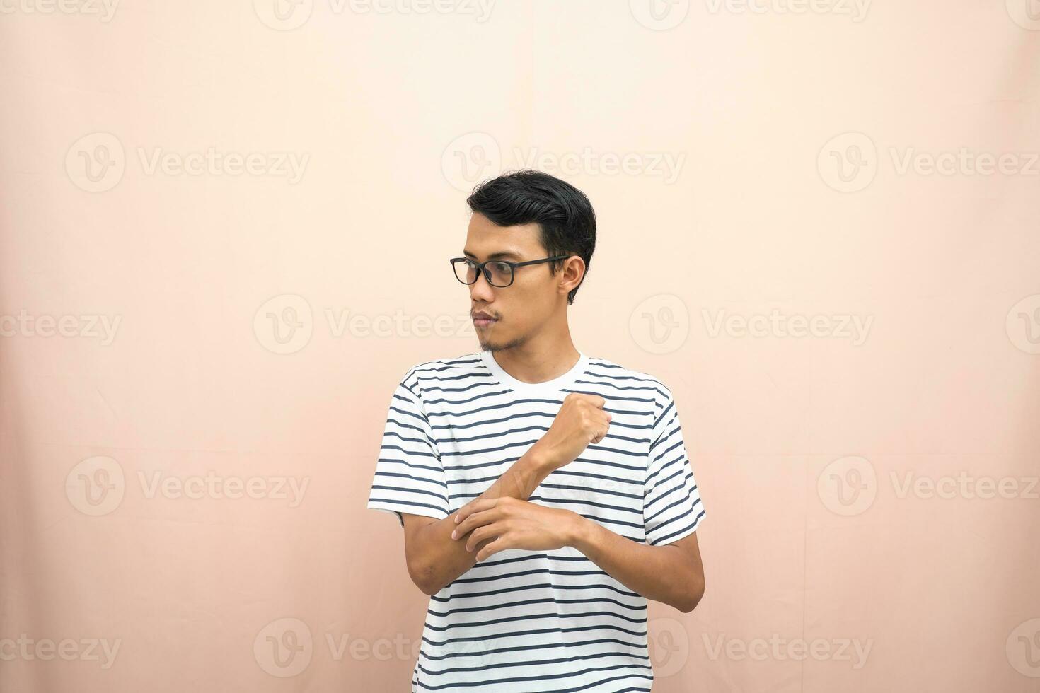 Asian man with glasses wearing casual striped shirt, fist fist pose, indicating strong or ready to fight. Isolated beige background. photo