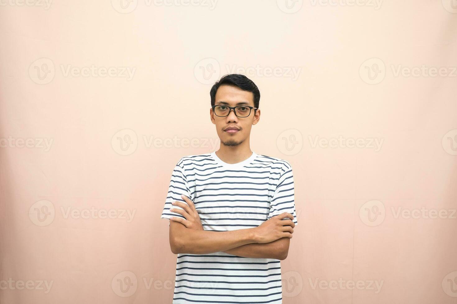 Asian man in glasses wearing casual striped shirt, standing pose with crossed arms, smiling and serious. photo