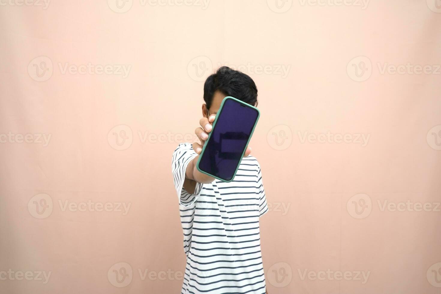 portrait of an asian man wearing glasses wearing a casual striped t-shirt. Shows smartphone screen with happy, surprised, happy expression, for promotion. Isolated beige background. photo