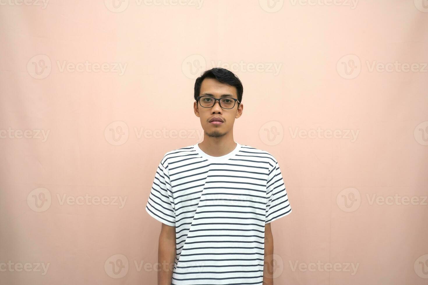 portrait of an asian man wearing glasses wearing a casual striped t-shirt. Stand up straight. Isolated beige background. photo