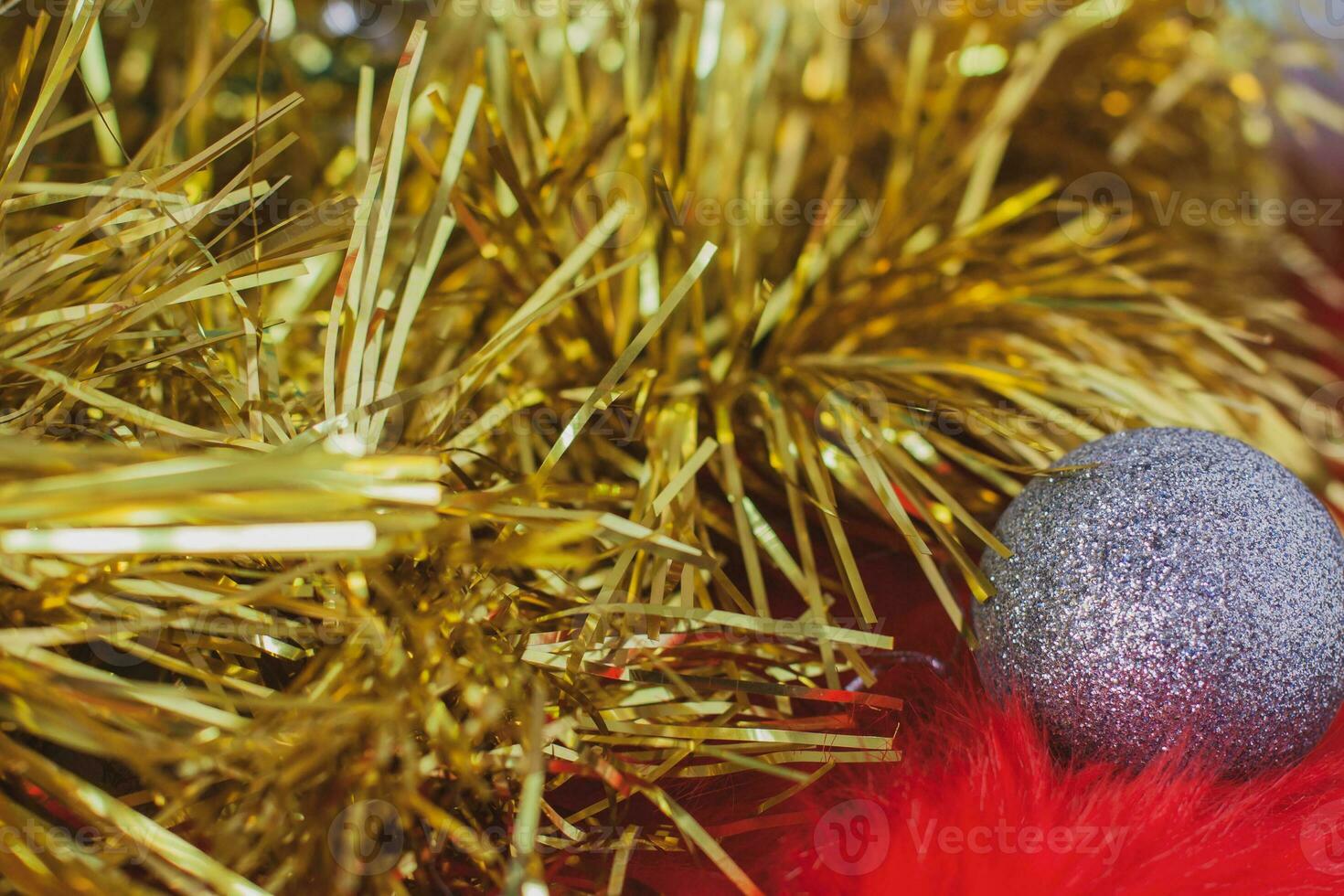 Christmas background of golden tinsel and Christmas silver ball on red fur. Fluffy fur with a long pile. Selective shallow focus on the ball. photo