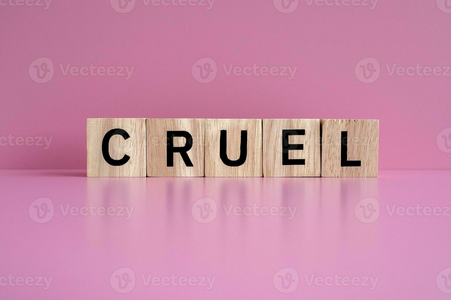 Wooden blocks form the text CRUEL against a pink background. photo