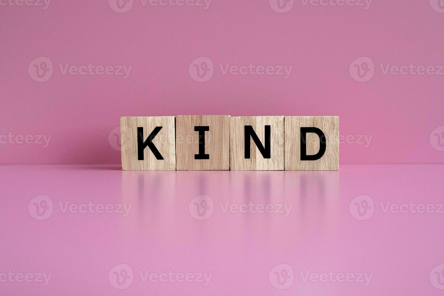 Wooden blocks form the text KIND against a pink background. photo