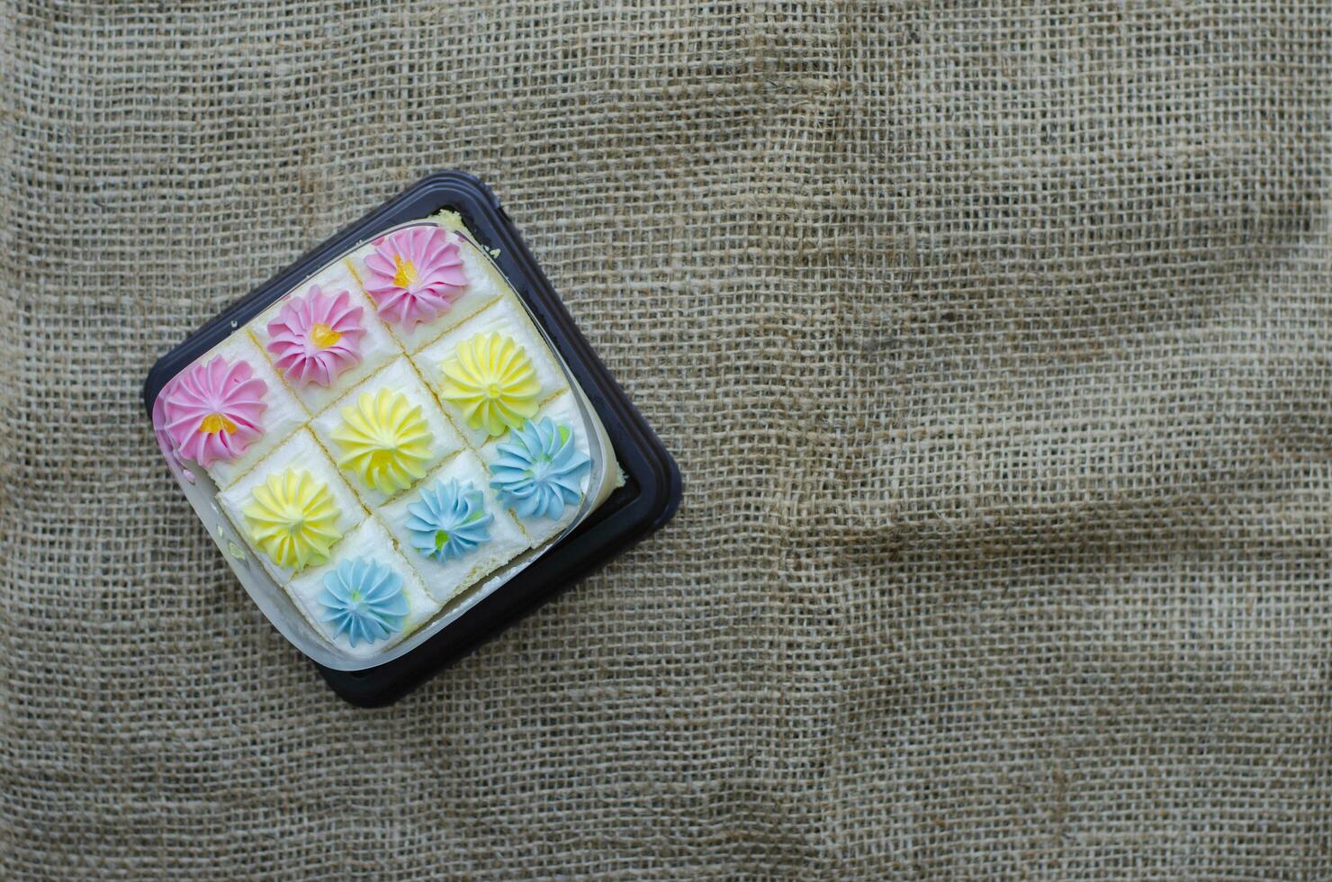 Fresh and delicious bento mini vanilla cupcakes with whipping cream pastel colors. on brown fabric background. Top view with copy space photo