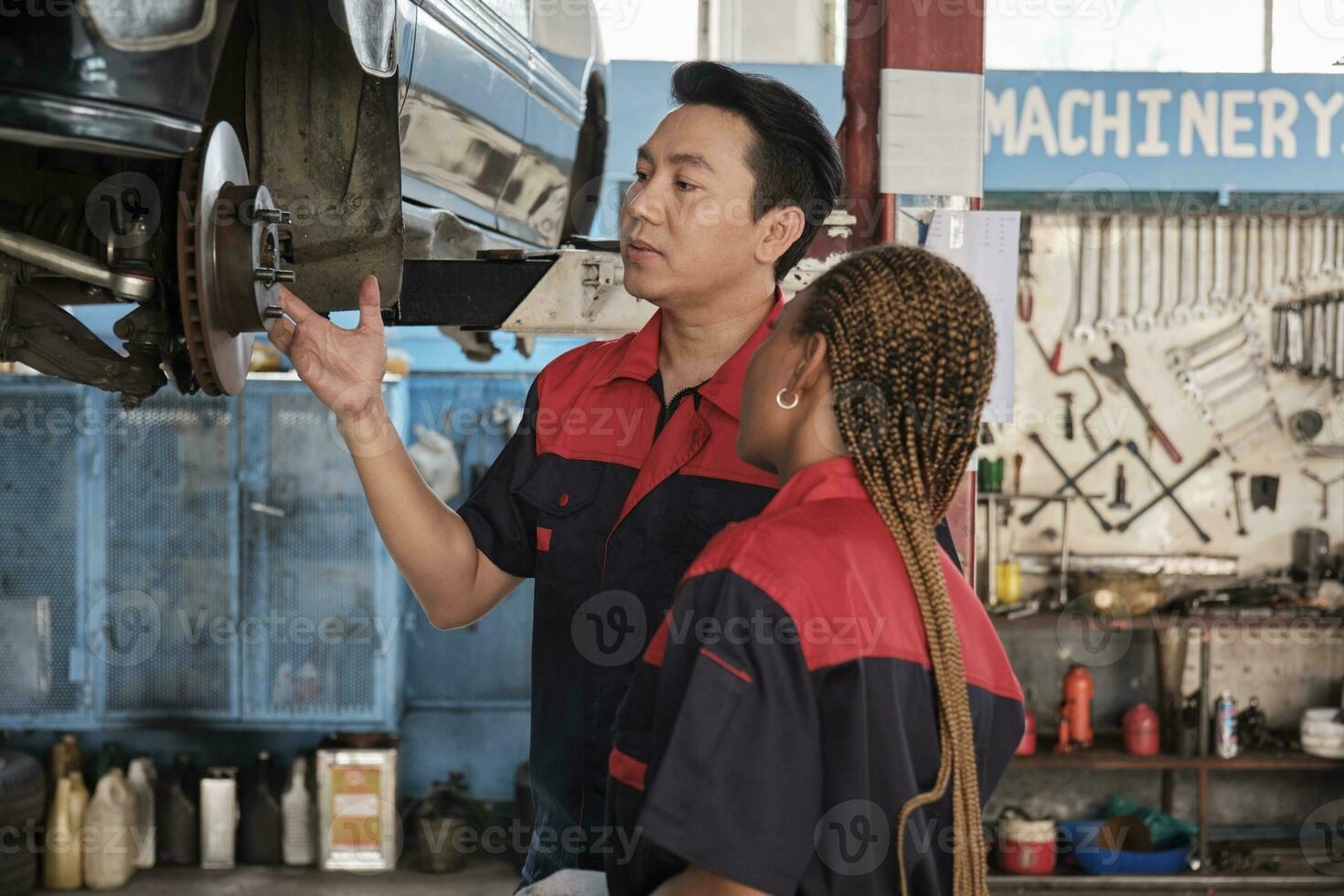 Professional automotive supervisors inspect and discuss car suspension repair work with female African American mechanic worker at service garage, and fix specialist occupations in the auto industry. photo