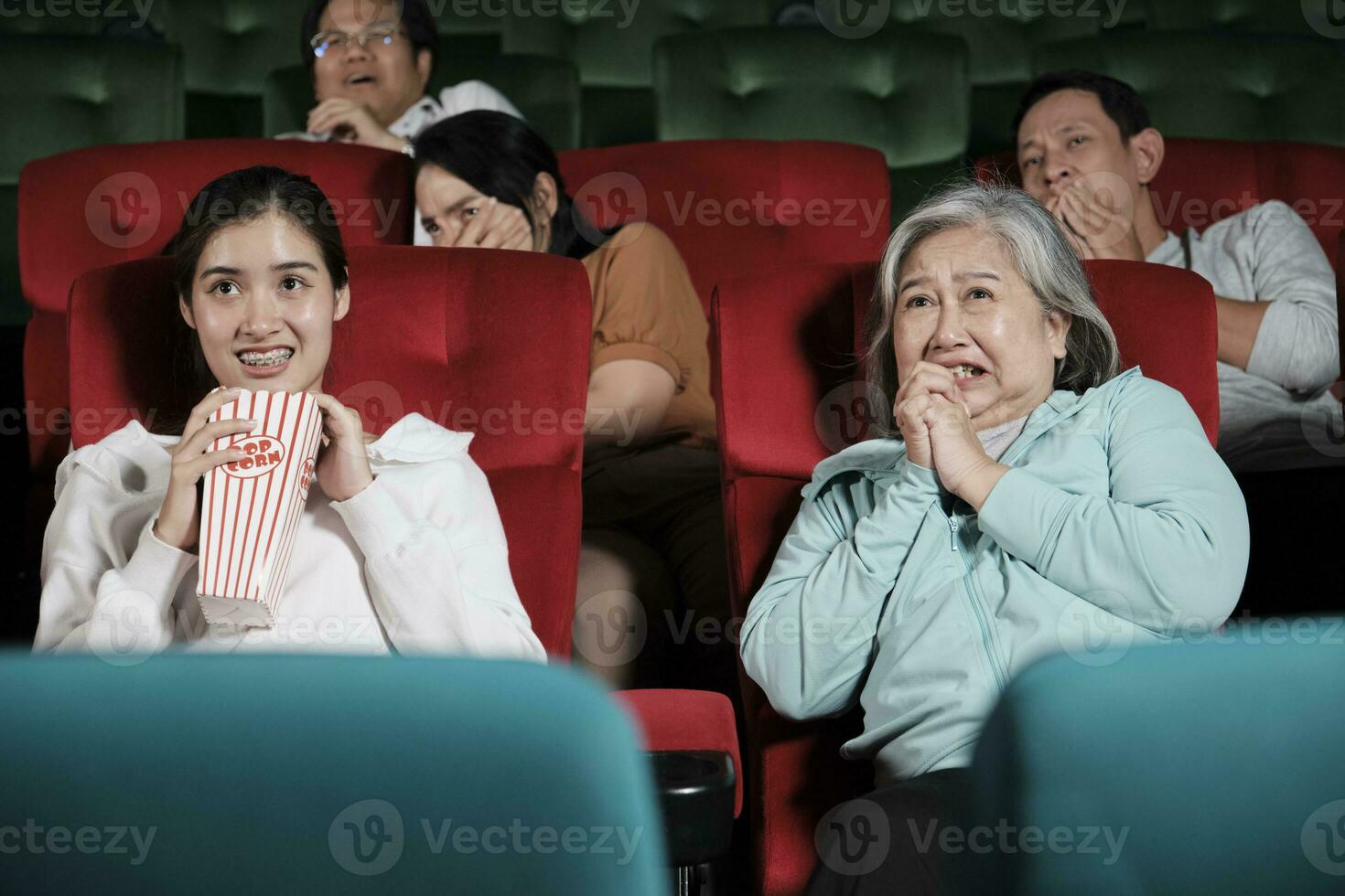 Various people in theater. Asian senior woman and many audiences are scared of watching thriller and horror cinema, frightened together on movie stage, and entertainment lifestyle with film show. photo