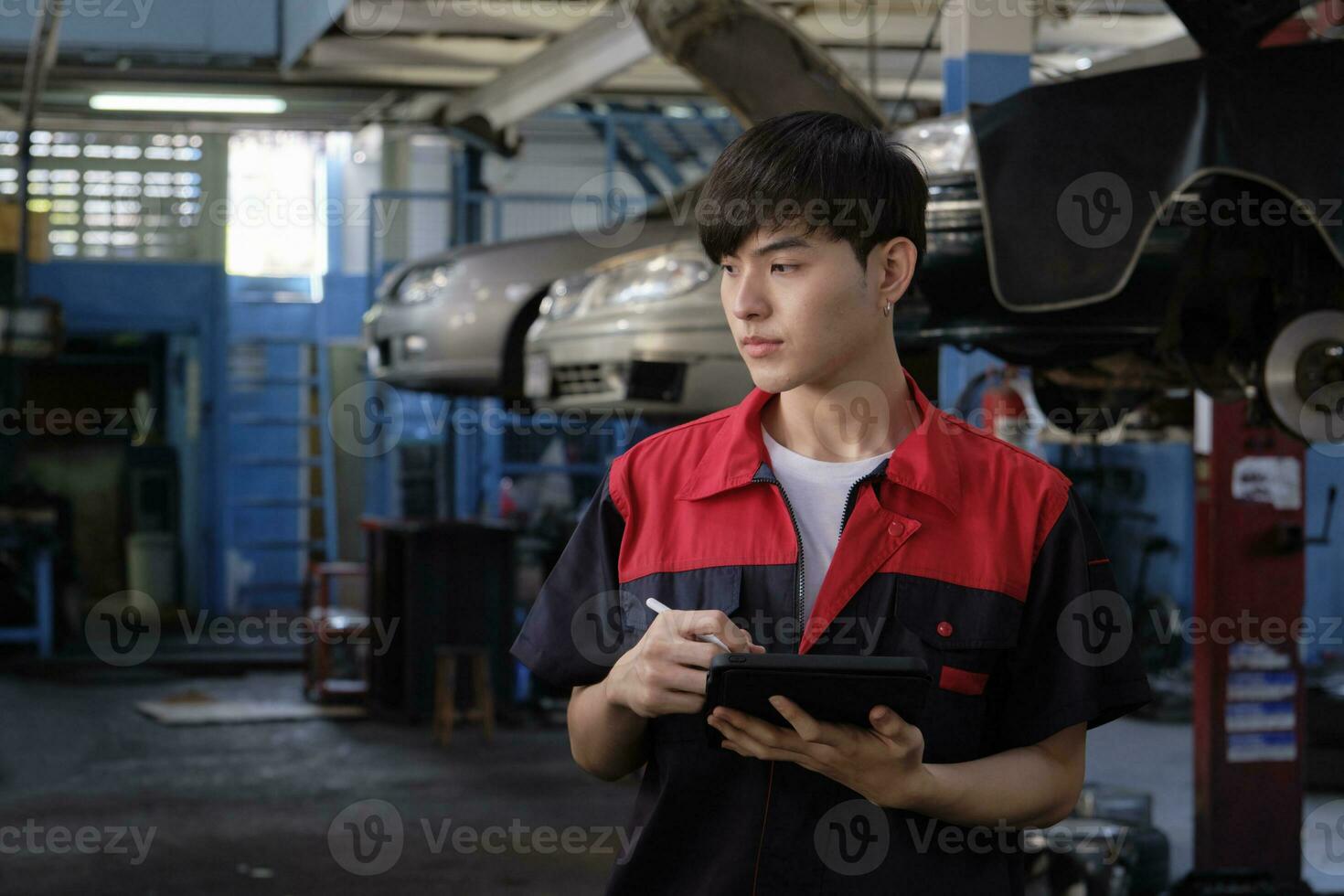 uno masculino asiático profesional mecánico, supervisor ingeniero, inspecciona reparar trabajo listas de verificación con tableta a cochera, Servicio coche mantenimiento, y fijación especialista ocupaciones en auto transporte industria. foto