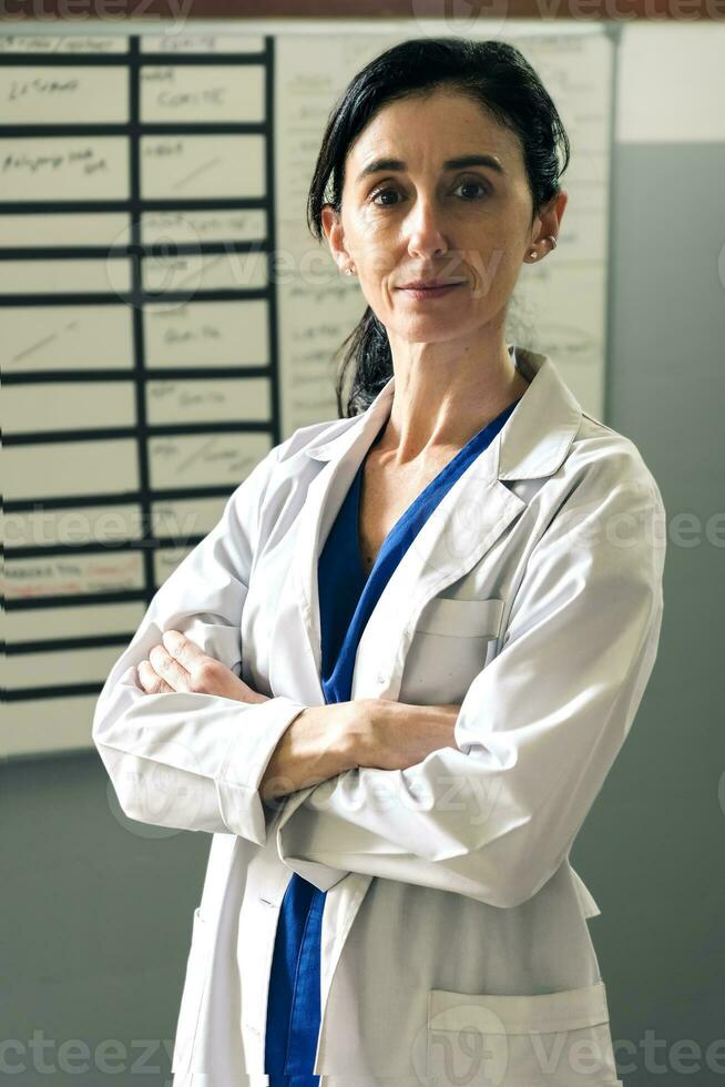 Positive female doctor in white uniform looking at camera and crossing her arms. photo