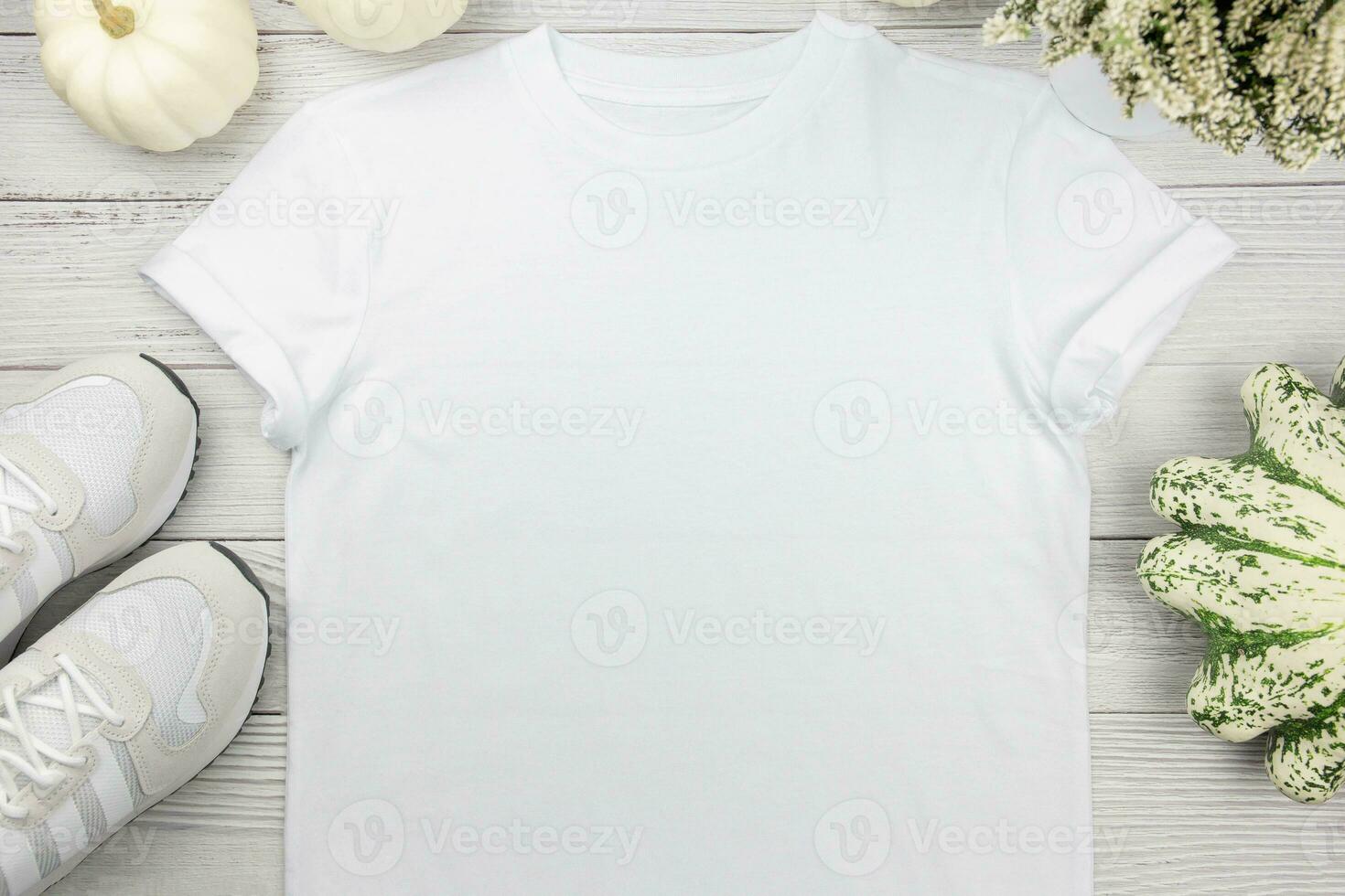 White womens cotton t-shirt mockup with pumpkins and sneaker on white wooden background. Design t shirt template, print presentation mock up. Top view flat lay. photo