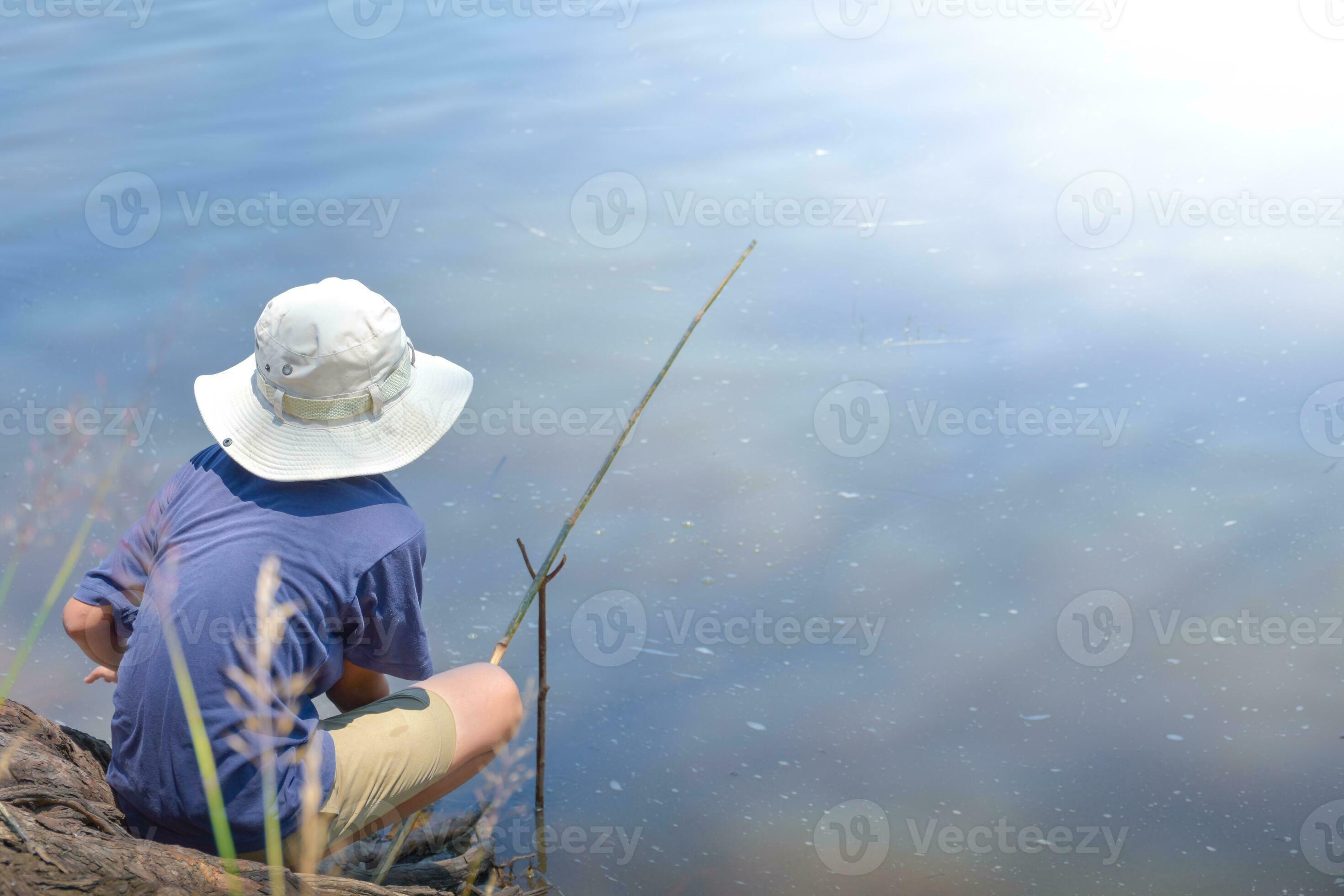 Asian young boy sitting fishing by river using bamboo fishing rod
