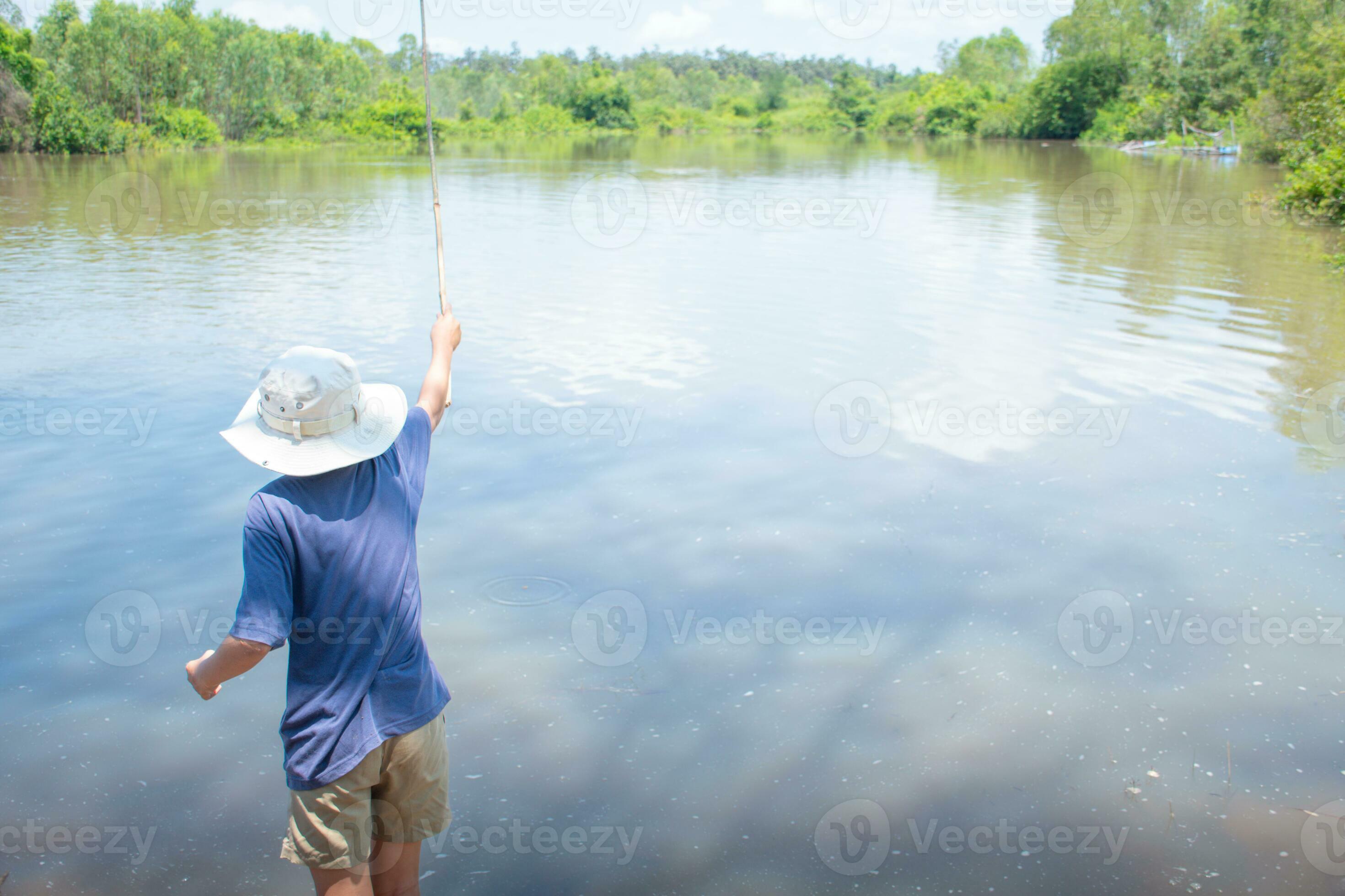 Asian boy standing fishing by river using bamboo fishing rod on