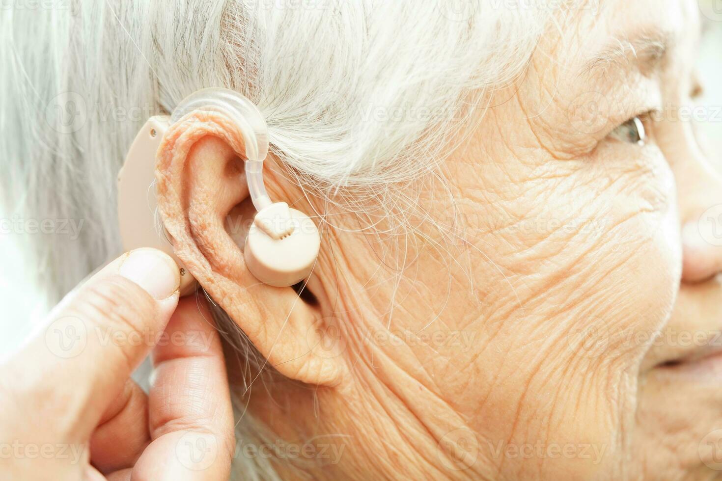 Doctor install hearing aid on senior patient ear to reduce hearing loss problem. photo