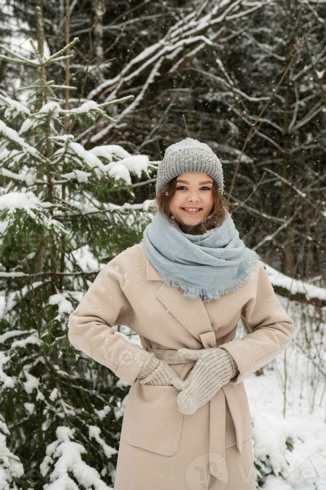 un linda niña es en pie debajo el nieve en el bosque en mitones y un Saco foto