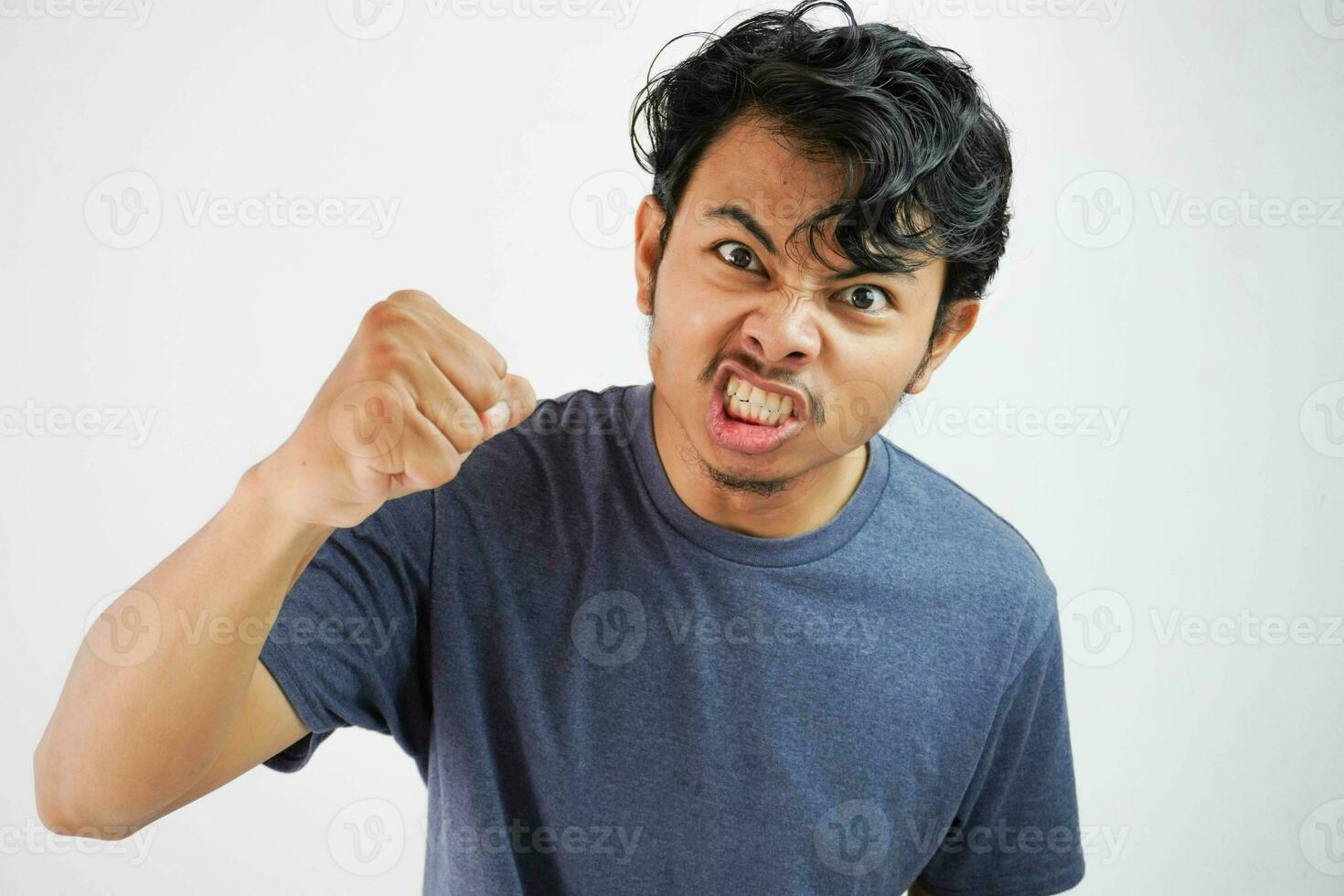 Angry aggressive young asian man wearing t shirt navy color shouting out loud with ferocious expression and mad raising fists frustrated photo