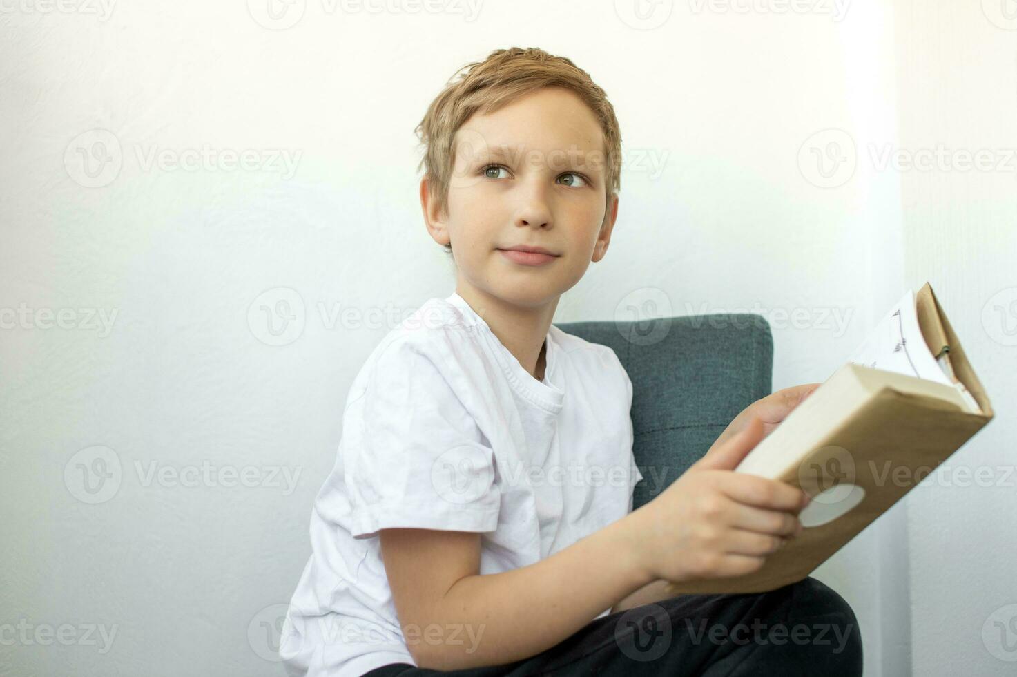 Cute boy reading a book while sitting on a chair and looking away photo