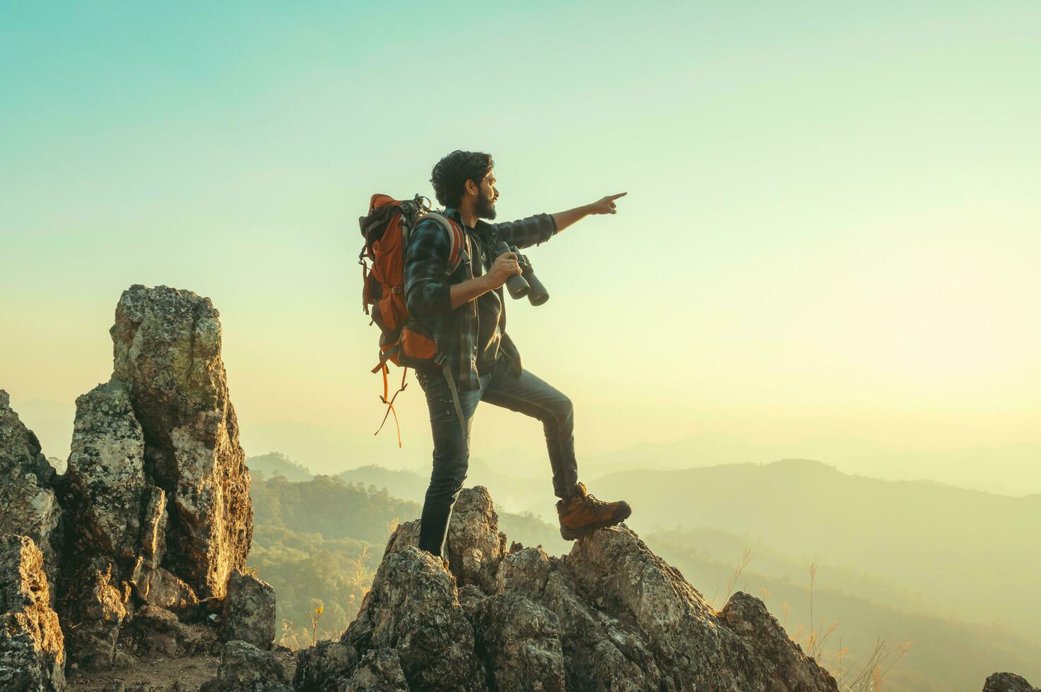 traveler with backpack and holding  binocular standing on top of mountain pointing at view photo