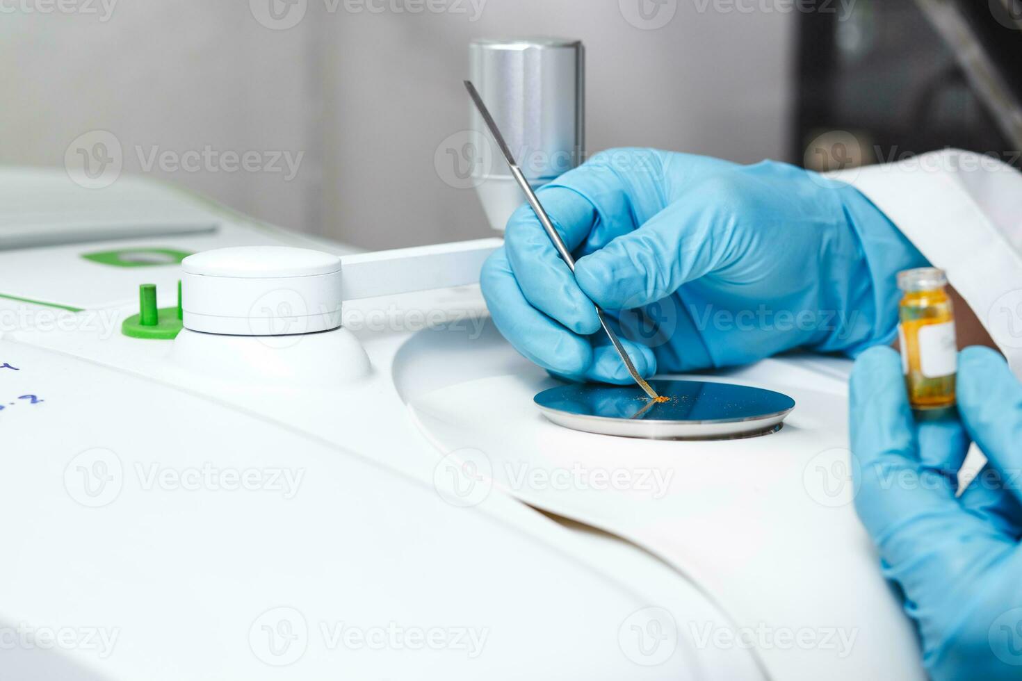Hand of scientist using a stainless spatula to scoop sample solid from vial to the Fourier Transform Infrared Spectroscopy FTIR pedestal instrument for substance analysis and chemical characterization photo