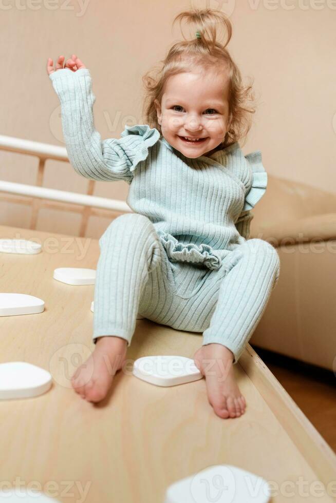 A little girl climbs a wooden slide in the gym. The child goes in for sports and develops photo