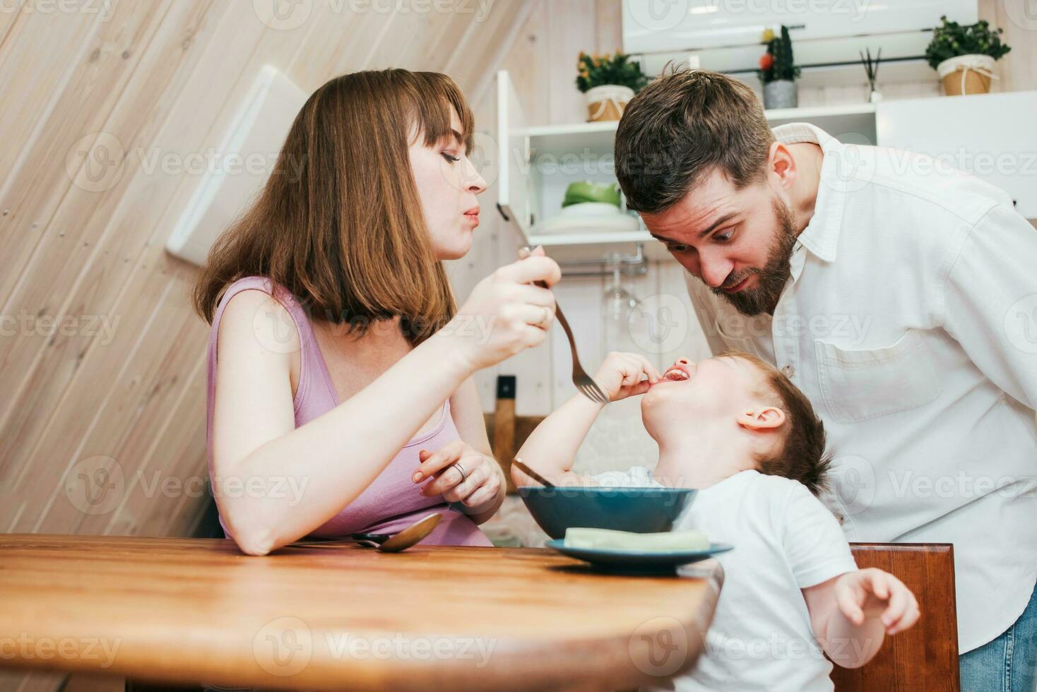 Mother with father feeding the child in the kitchen with pasta photo