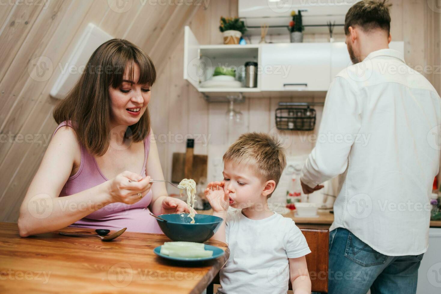 Happy child eats pasta in the kitchen with her family photo