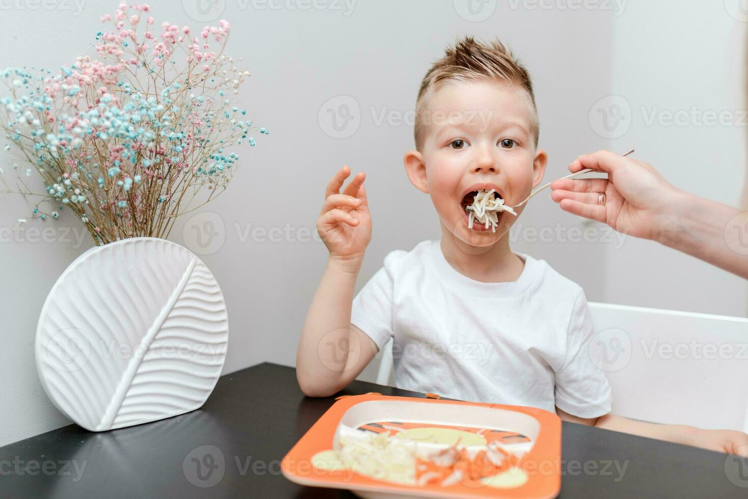 Happy child eating delicious pasta at the table in the kitchen photo