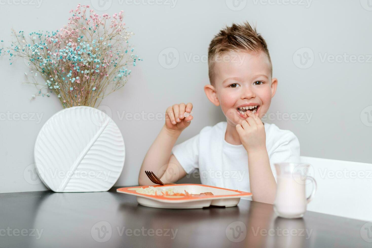 Laughing boy eats delicious pasta at the table in the kitchen photo