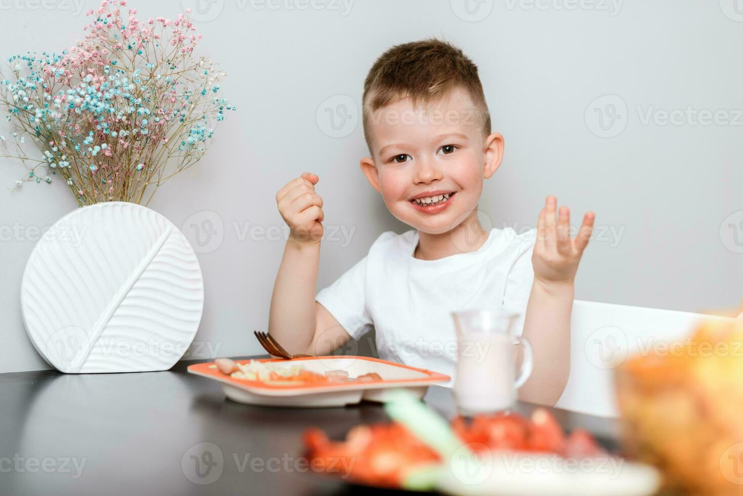 Laughing boy eats delicious pasta at the table in the kitchen photo