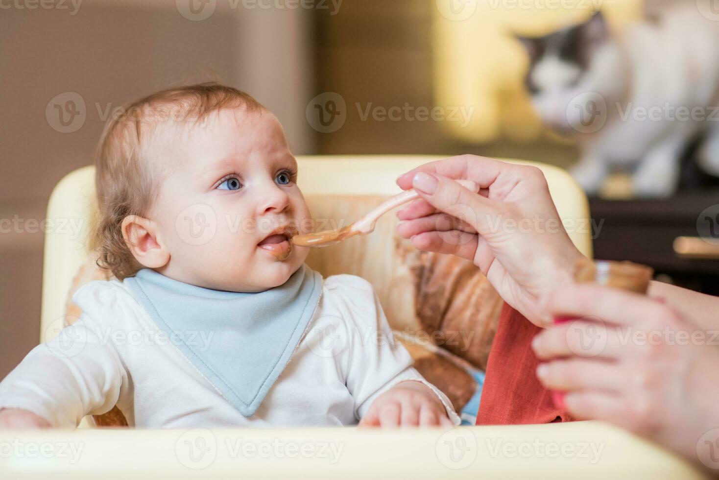 Mom feeds a happy baby fruit puree from a spoon. First food photo