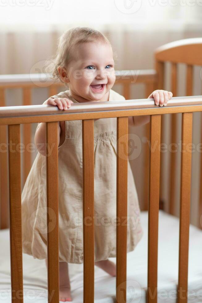 contento y riendo pequeño niña jugando en su cuna en el dormitorio foto