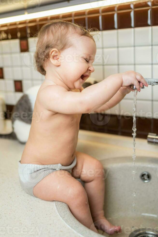 Laughing little girl takes hygiene procedures in the washbasin in the kitchen photo