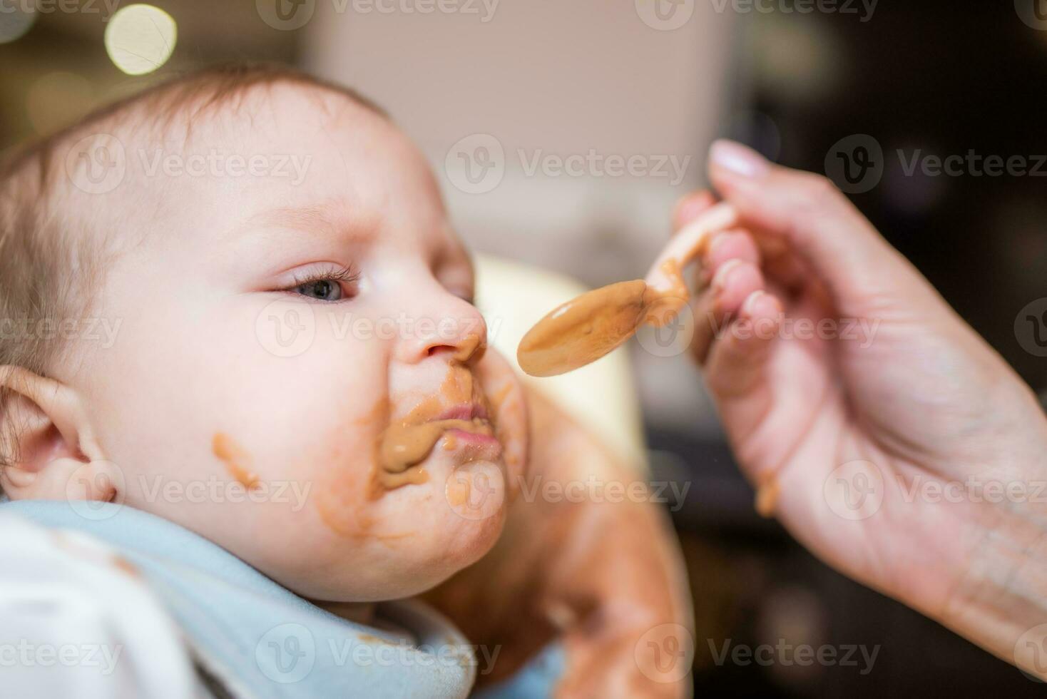 Happy mother feeding her cute little daughter fruit puree from a spoon. First food photo