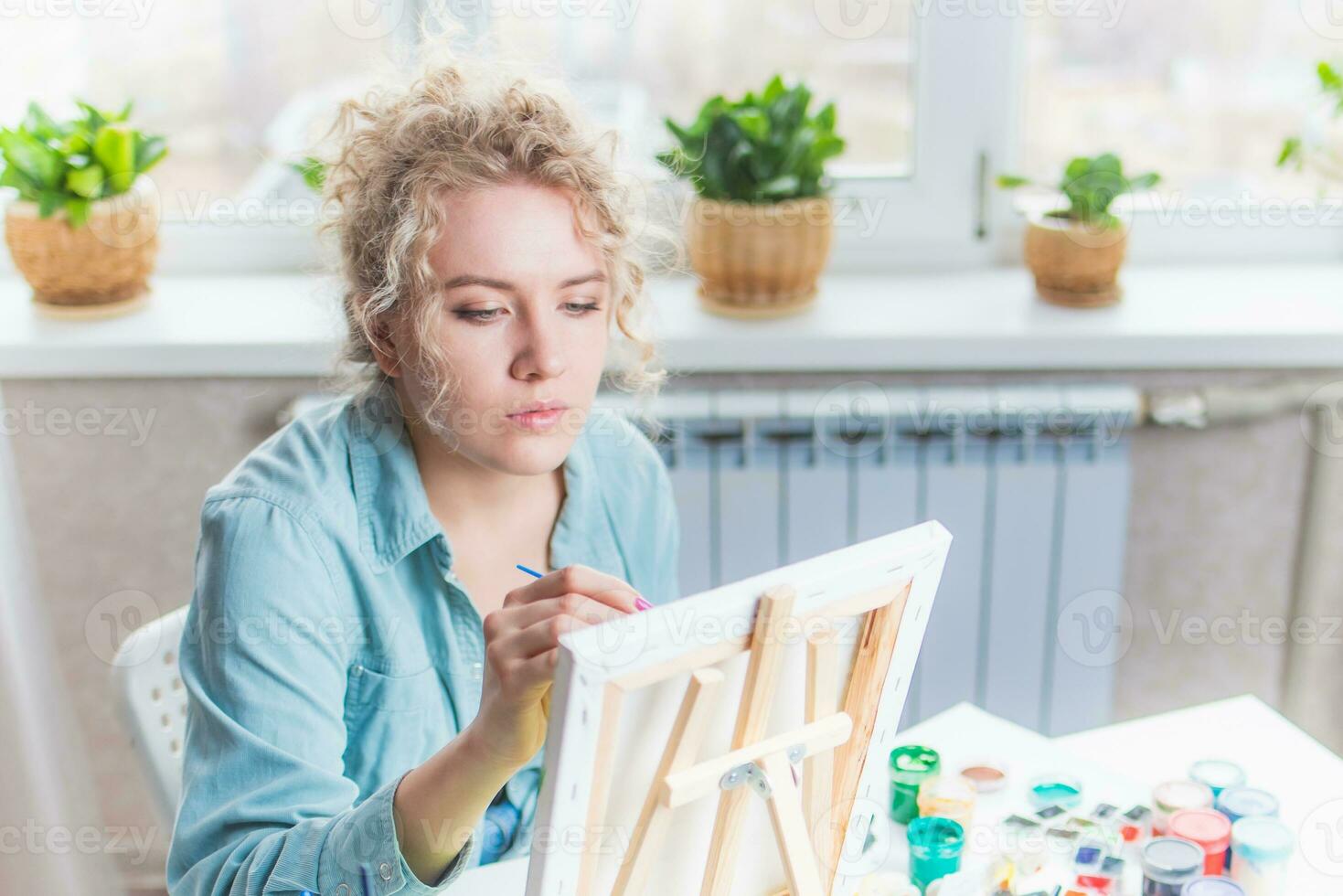 Curly blonde woman painting a picture by the window photo