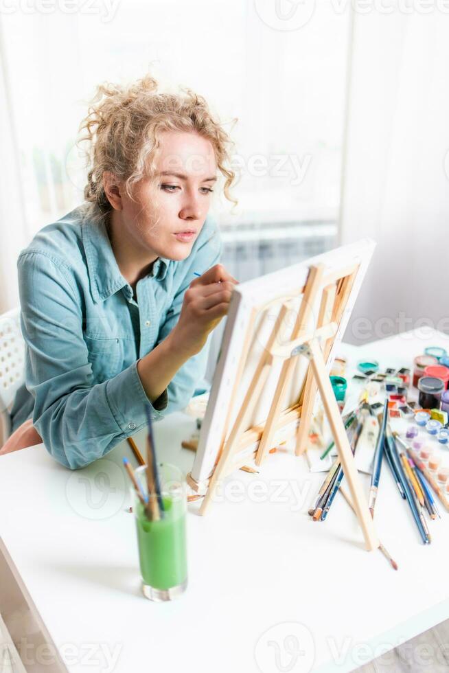 Curly blonde woman painting a picture by the window photo