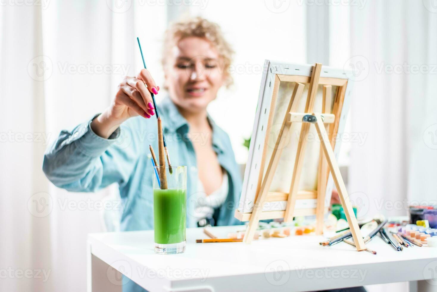 Curly blonde woman painting a picture by the window photo