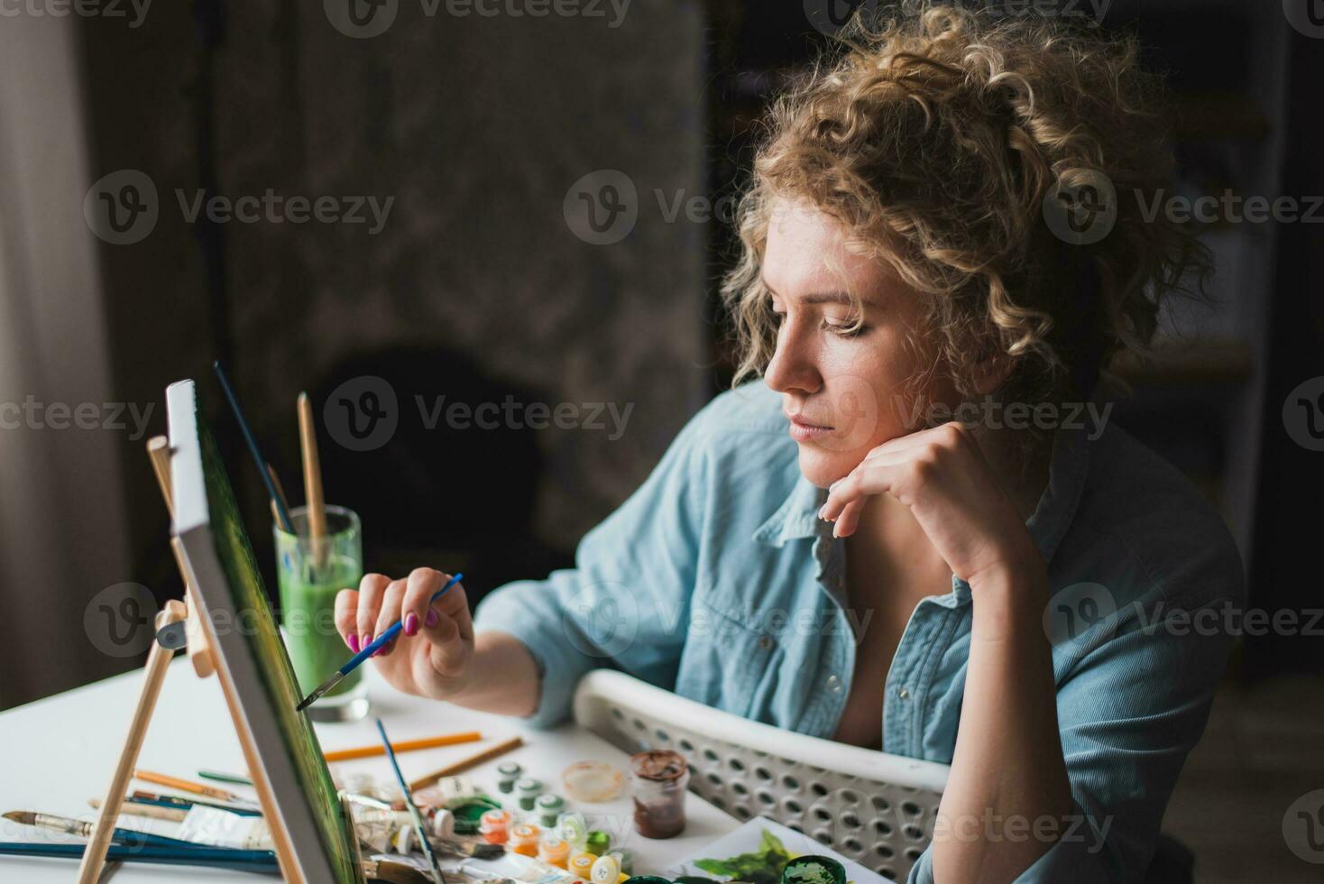 Curly blonde woman painting a picture by the window photo