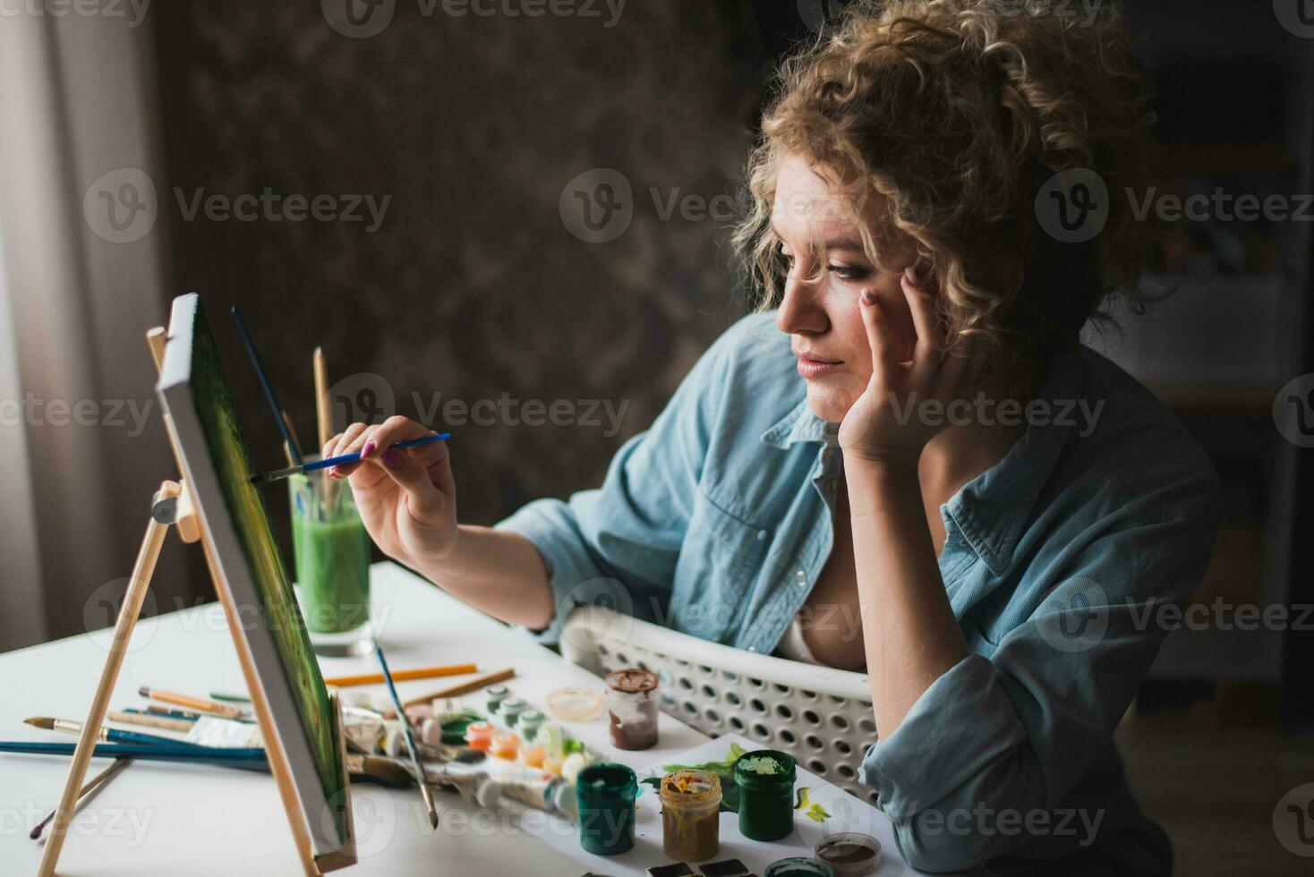 Curly blonde woman painting a picture by the window photo