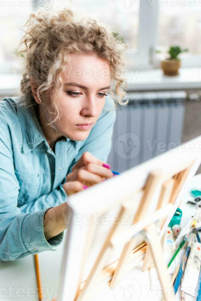 Curly blonde woman painting a picture by the window photo