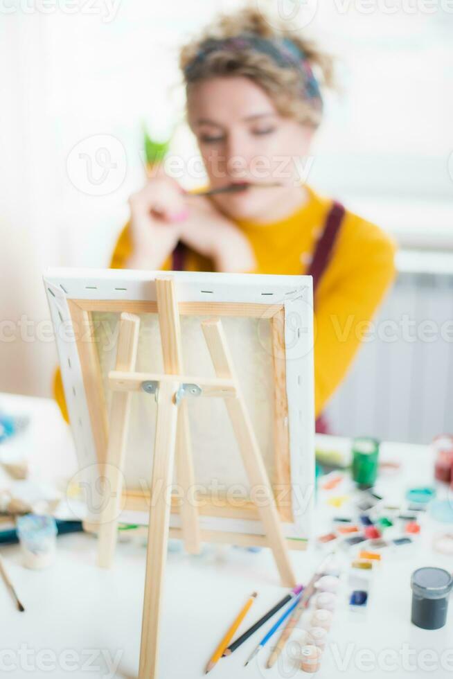 Woman sitting in front of a painting and painting with brushes on canvas at home photo