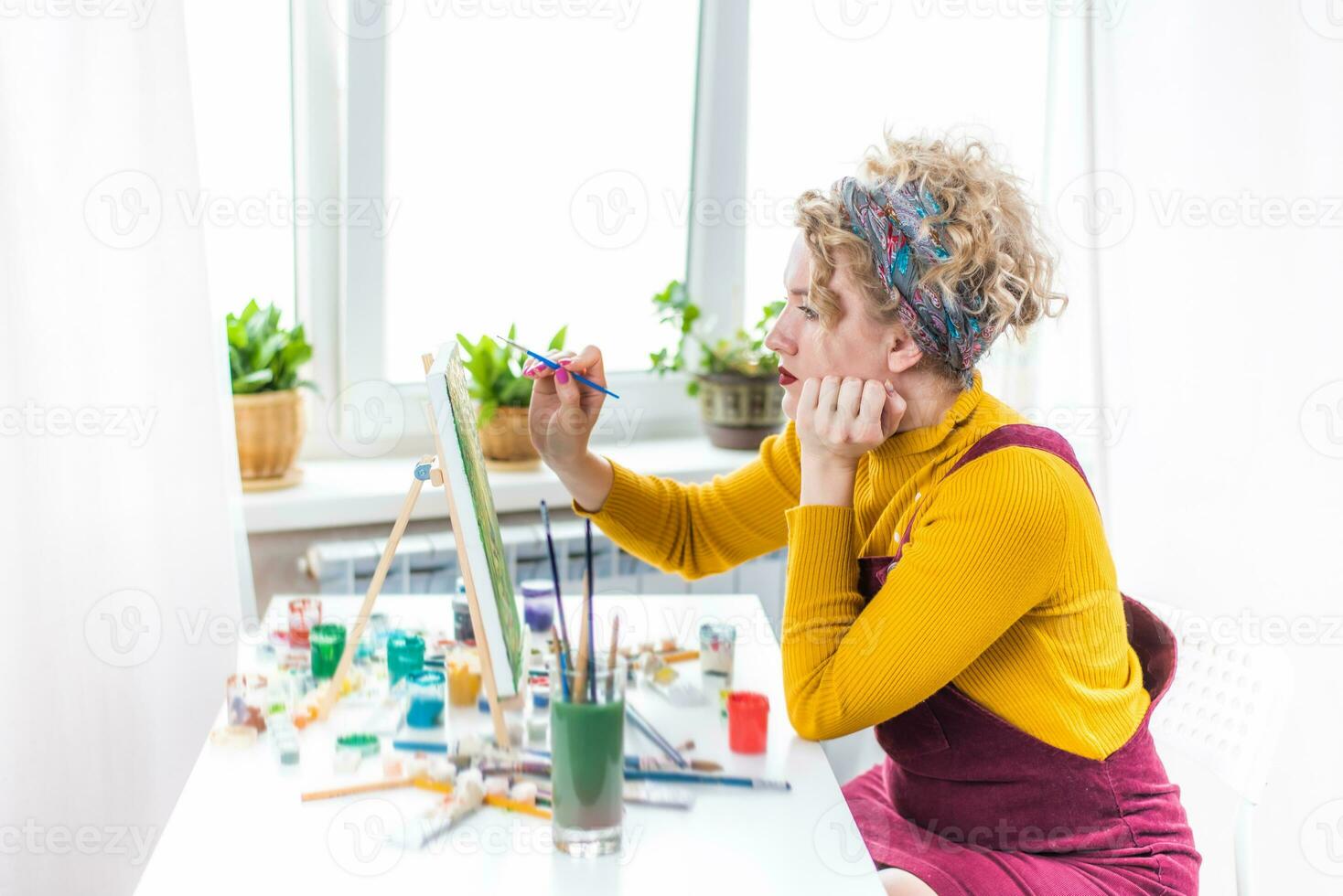 Curly blonde woman painting a picture by the window photo