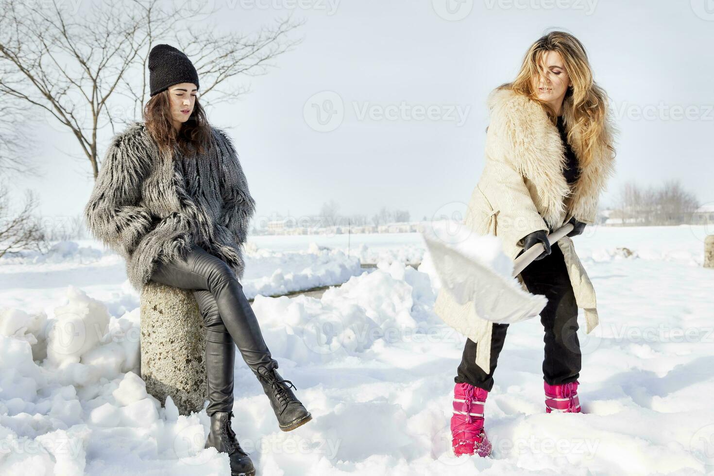 young women shoveling snow near a small wood photo