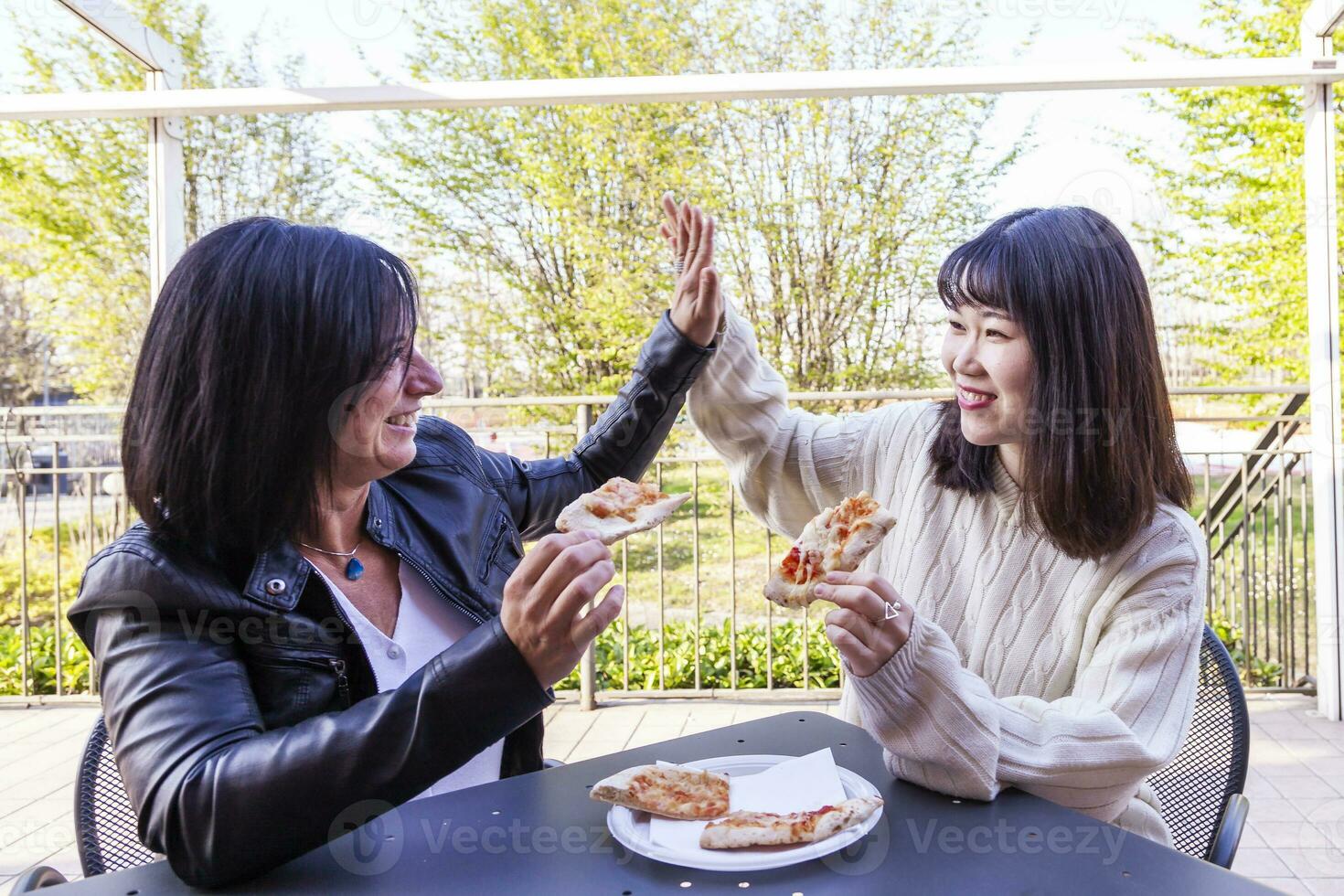 young multi-ethnic female friends eating a pizza outdoors photo