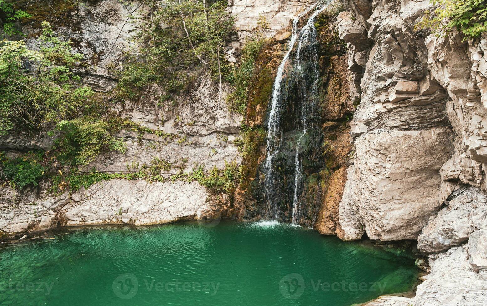 wonderful small waterfall that forms a pond of emerald water in a forest photo