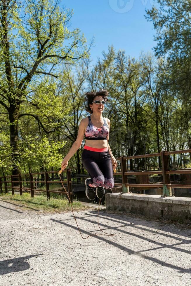 hermosa medio Envejecido mujer saltando cuerda al aire libre foto