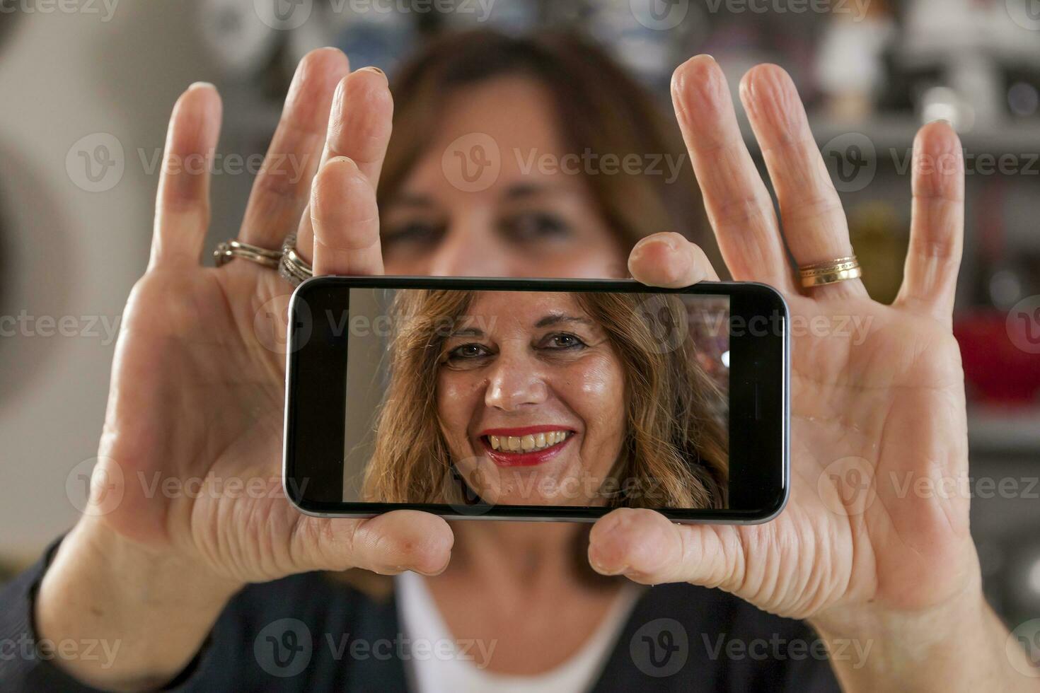 hermosa contento medio Envejecido mujer tomando un selfie con teléfono inteligente en el cocina foto