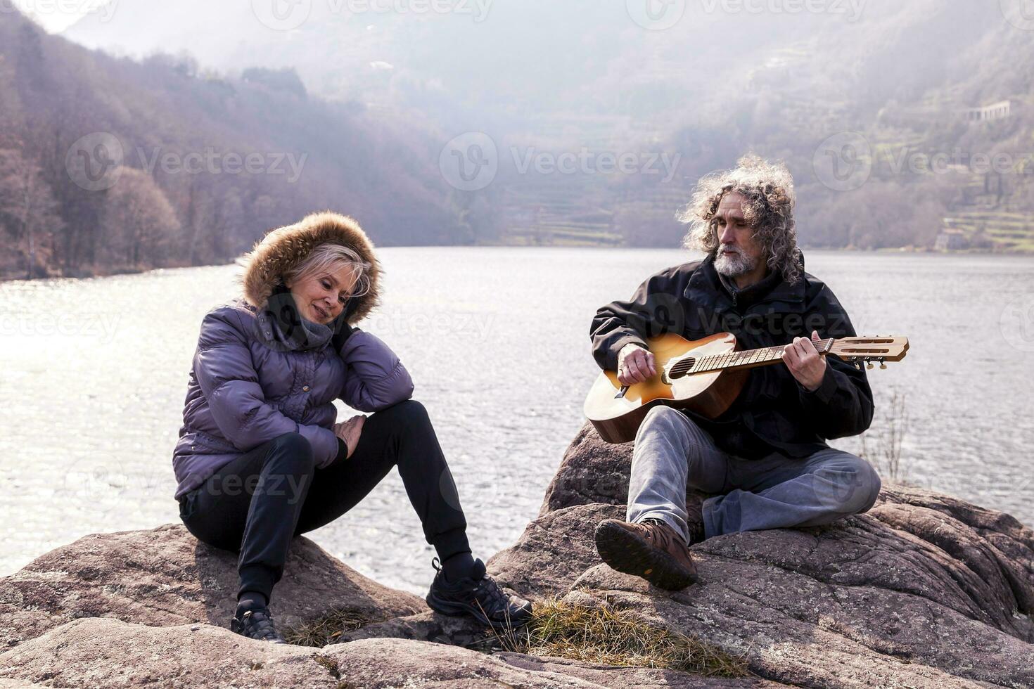beautiful mature couple playing a guitar sitting on the lake photo