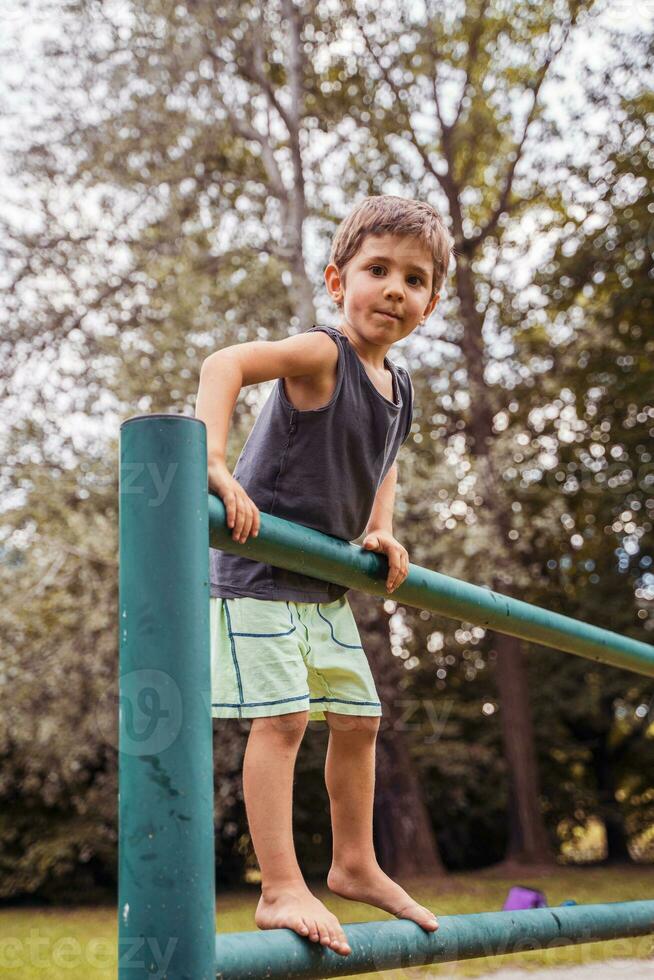 sonriente linda niño alpinismo en un metal barandilla en un público parque foto