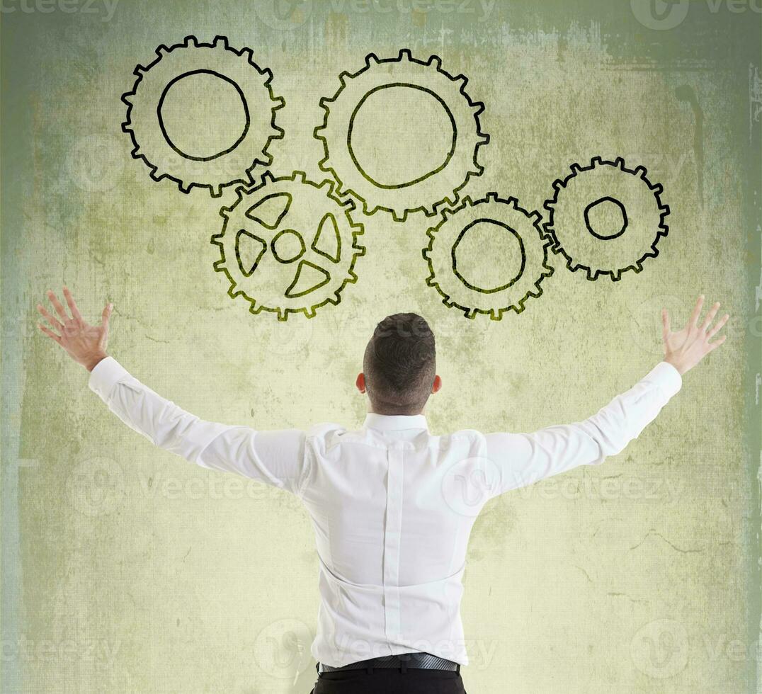 young businessman looks at gear symbols painted on the wall photo